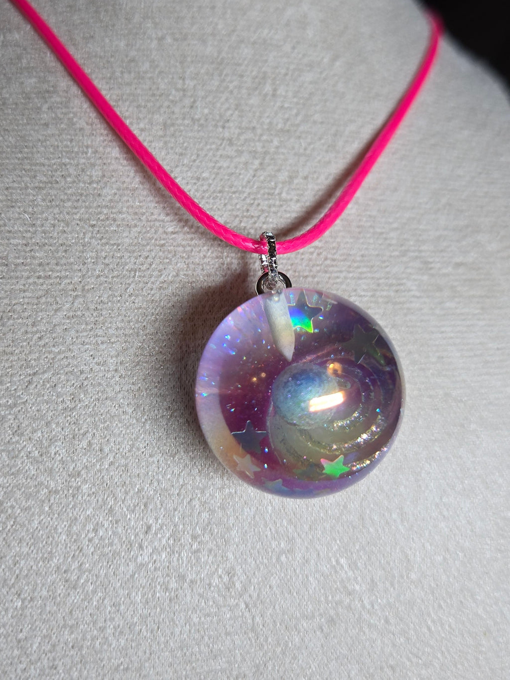 A round iridescent purple resin bead pendant on a bright pink cord, displayed on a white fabric jewelry bust.